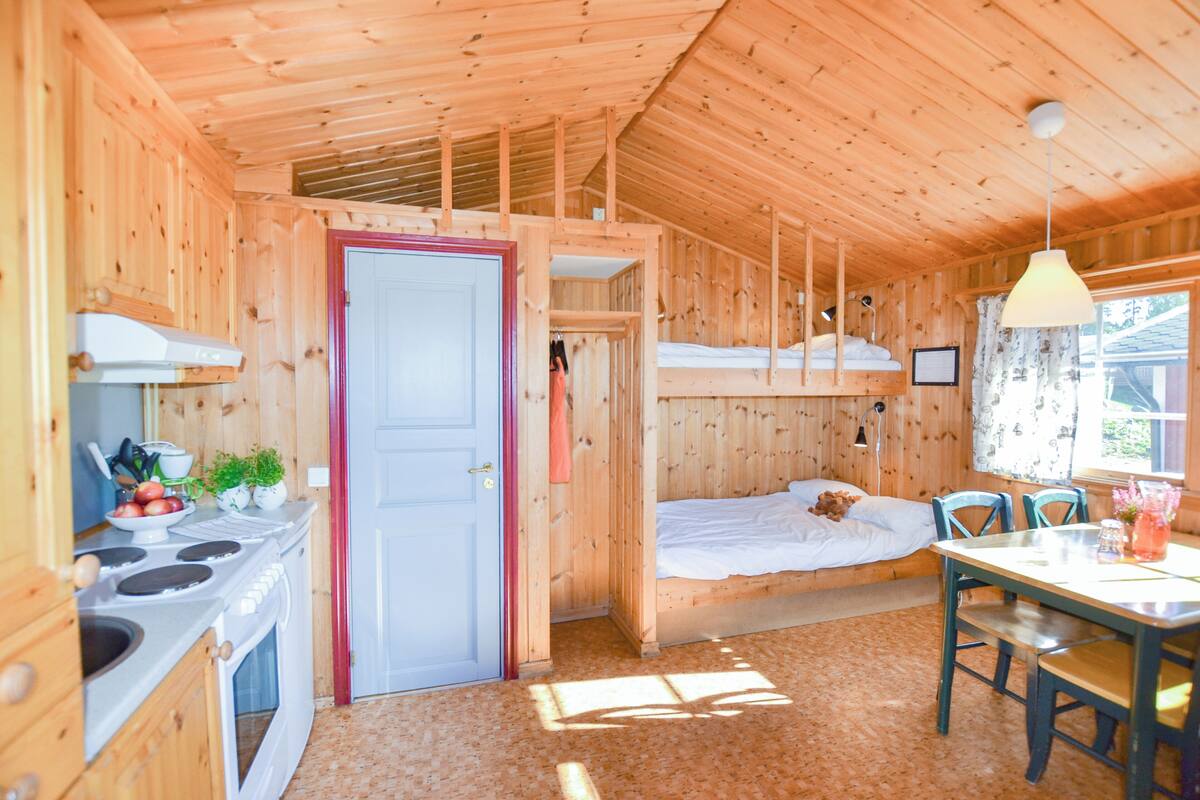 A wooden cabin with a kitchen, a dining area, and a sleeping loft.