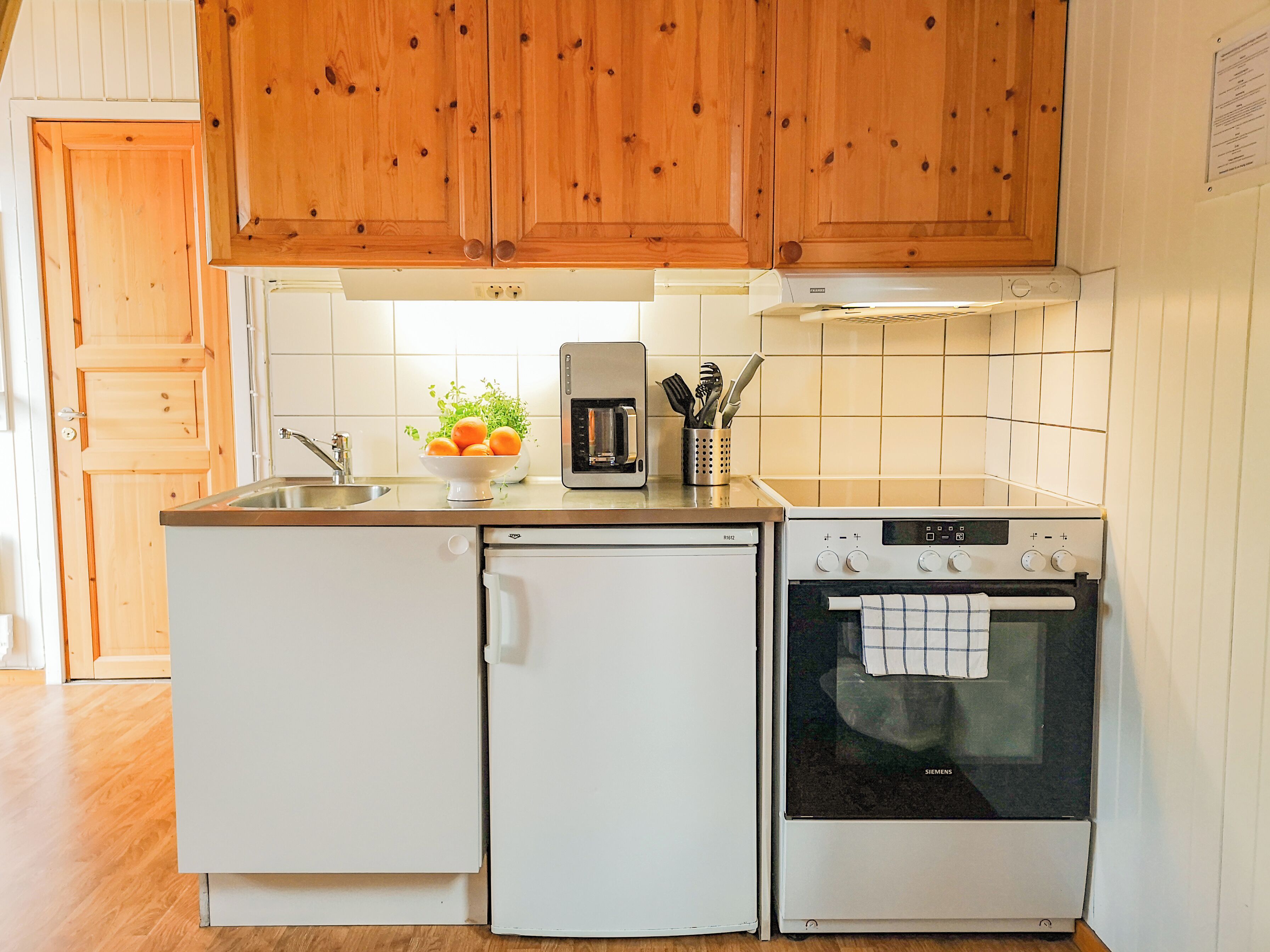 A compact kitchen with wooden cabinets, a built-in oven, a refrigerator, and a coffee maker.