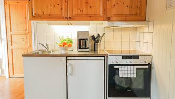 A compact kitchen with wooden cabinets, a built-in oven, a refrigerator, and a coffee maker.