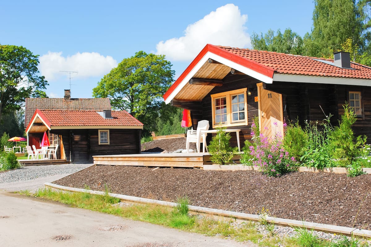 A wooden cabin with a red-tiled roof, a porch with outdoor seating, and a well-maintained garden.