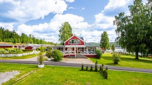 Un bâtiment rouge abritant la réception, doté d’un porche blanc et entouré d’une végétation luxuriante et d’un lac.