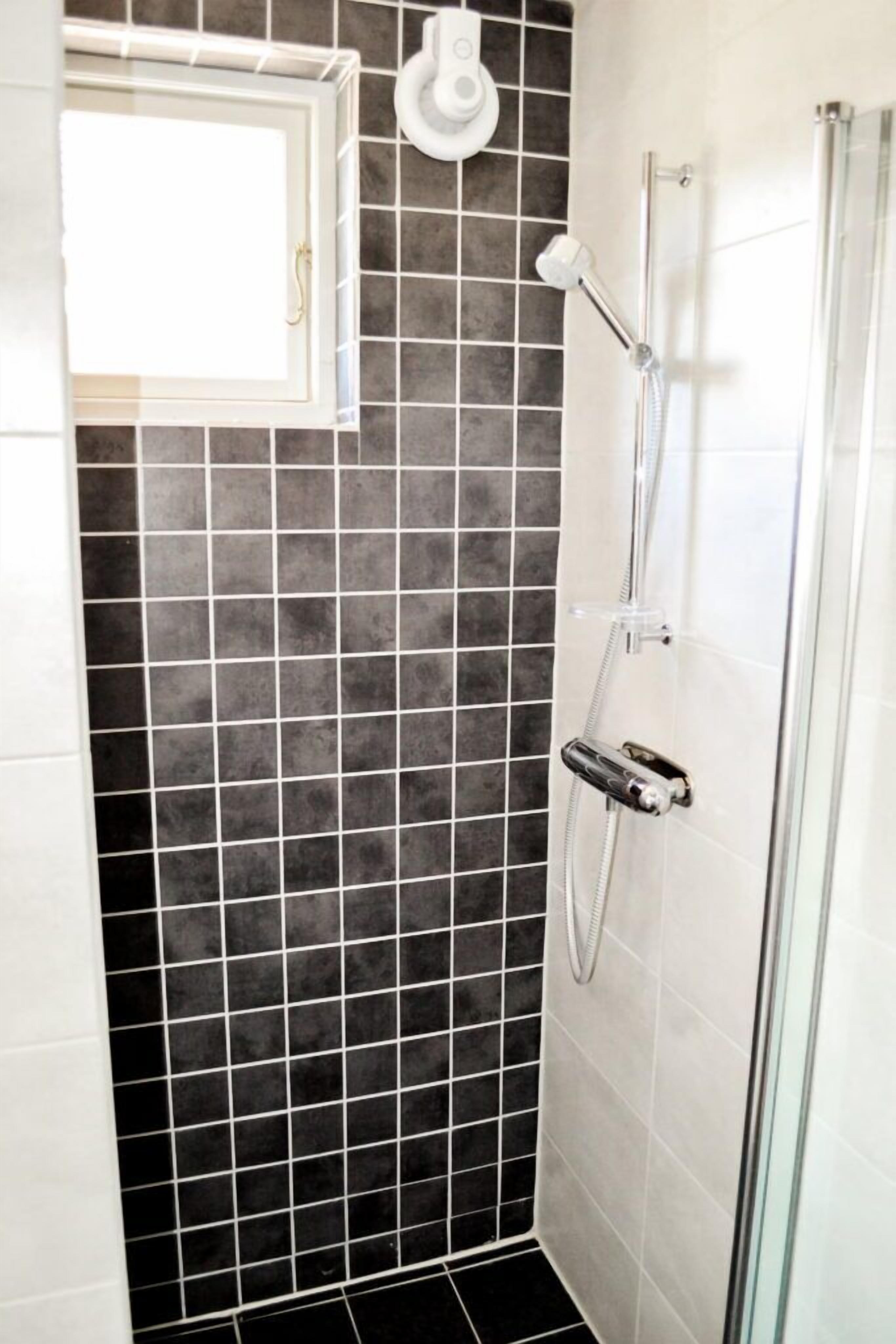 A shower with a glass door, a handheld showerhead, and a wall-mounted faucet.