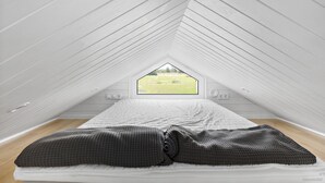A bedroom with a sloped ceiling, a bed with a white mattress and gray bedding, and a window with a view of a green field. - First Camp Vadstena - Vättern (Vadstena)