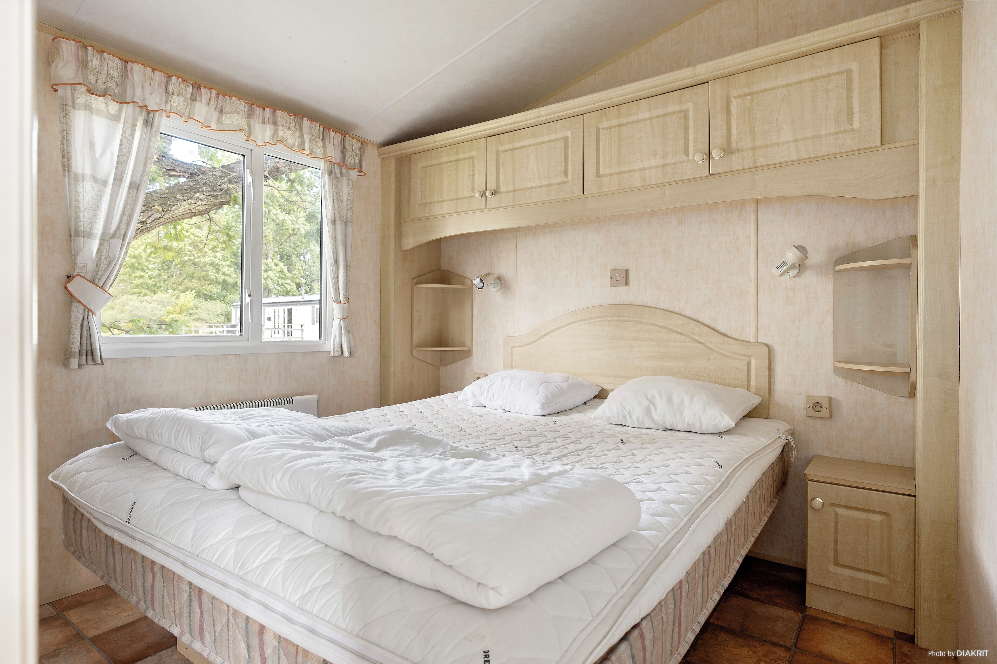 Un dormitorio con cama, armarios empotrados, una ventana con cortinas y vistas a árboles.