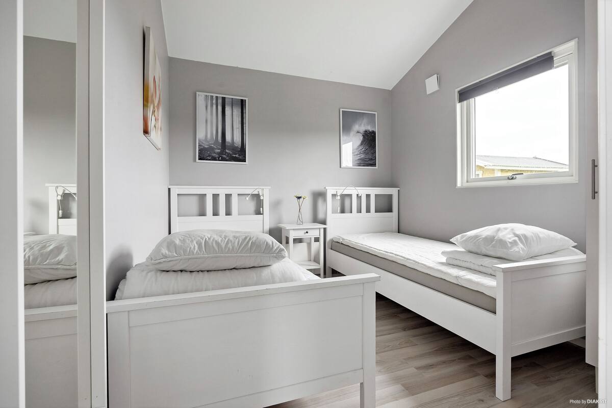 A bedroom with a bunk bed, a single bed, a bedside table, a mirror, and two framed pictures on the wall.