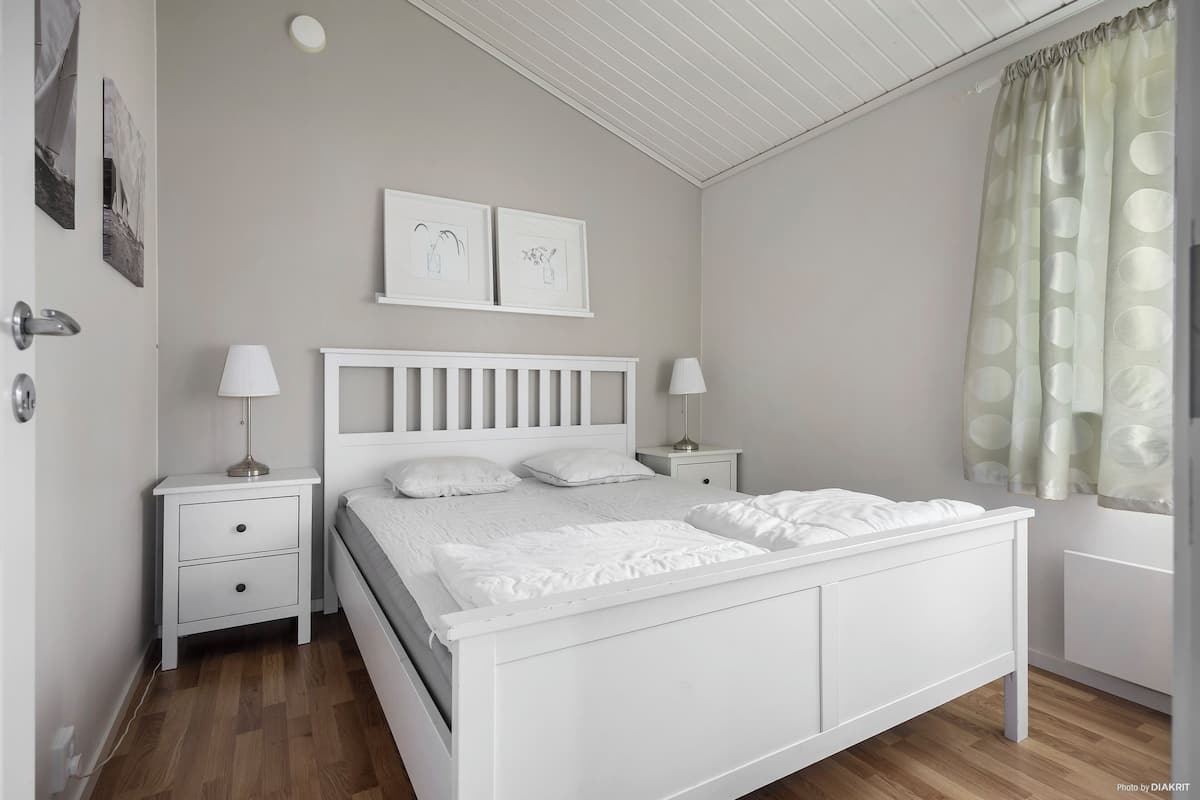 A white bedroom with a bed, nightstands, and a window with curtains.