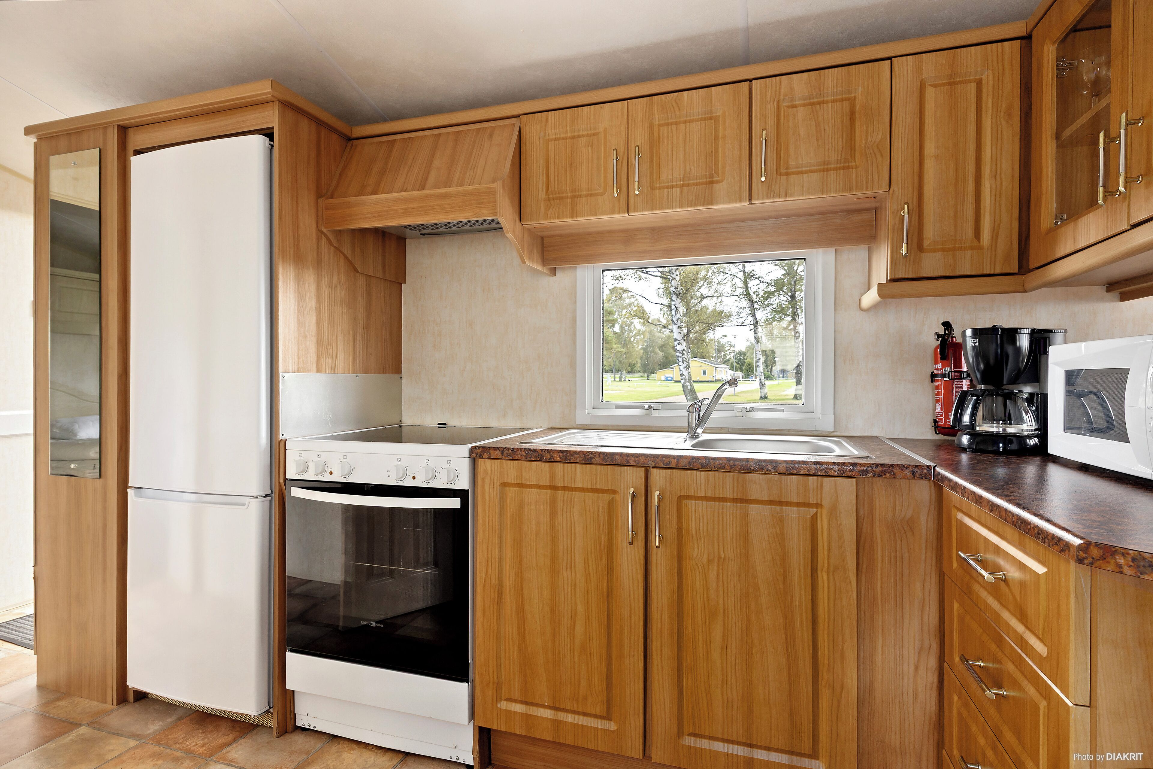 A kitchen with wooden cabinets, a refrigerator, stove, oven, and a window providing a view of the outdoors.