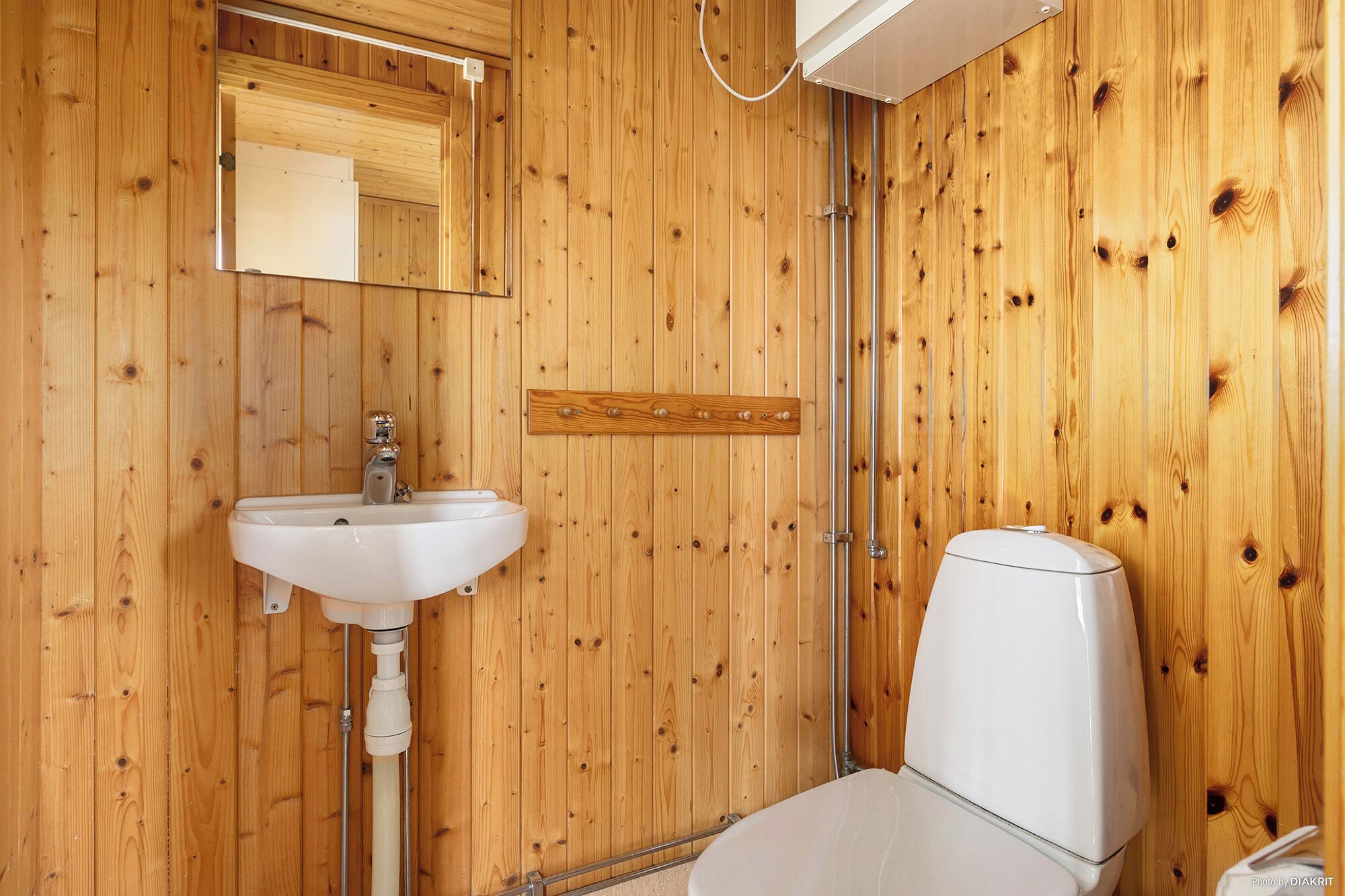 Un baño con paneles de madera, un lavamanos blanco, un espejo y un inodoro.