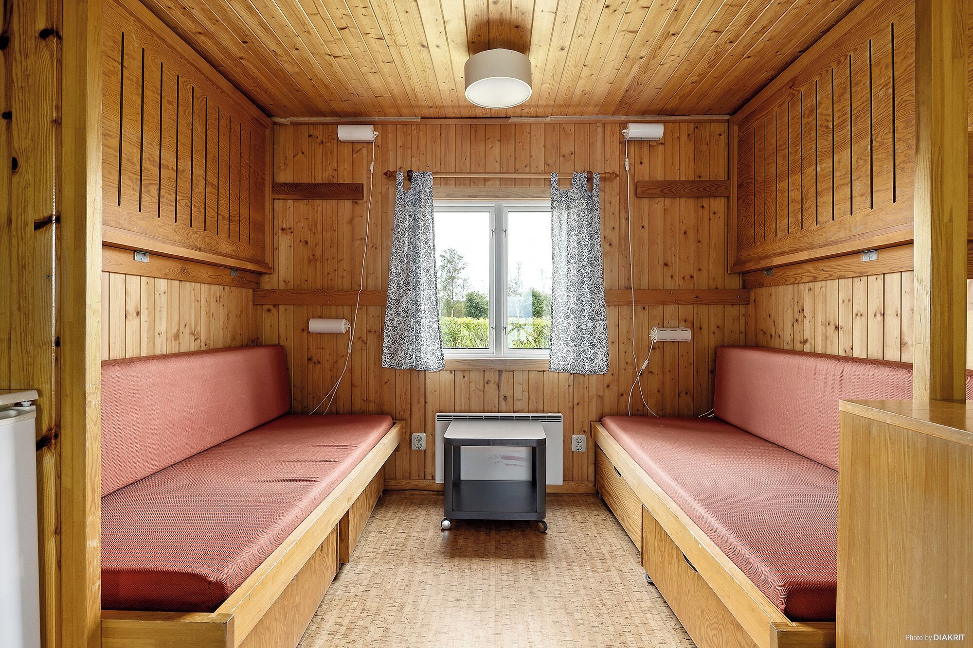 A cabin with two wooden bunk beds, a small heater, and a window with patterned curtains.