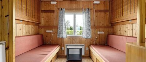 A cabin with two wooden bunk beds, a small heater, and a window with patterned curtains.