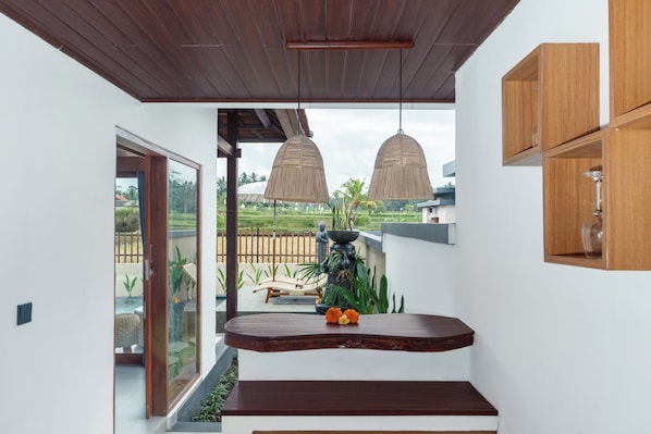 Un espacio exterior moderno con techo de madera, puerta de vidrio que da a un jardín y un banco de madera con un jarrón de flores.