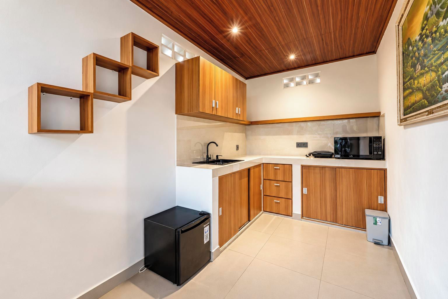 A compact kitchen with wooden cabinets, a black refrigerator, and a microwave on the countertop.