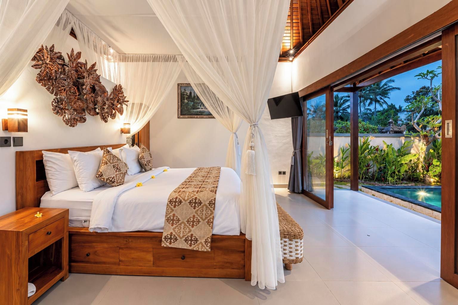 Ein Schlafzimmer mit einem großen Bett, einem Fernseher und Blick auf einen Swimmingpool.