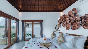 A spacious bedroom with a large bed, a decorative wall art piece, and a view of the outdoors. - Mahayani Ubud Villa (Tegallalang)