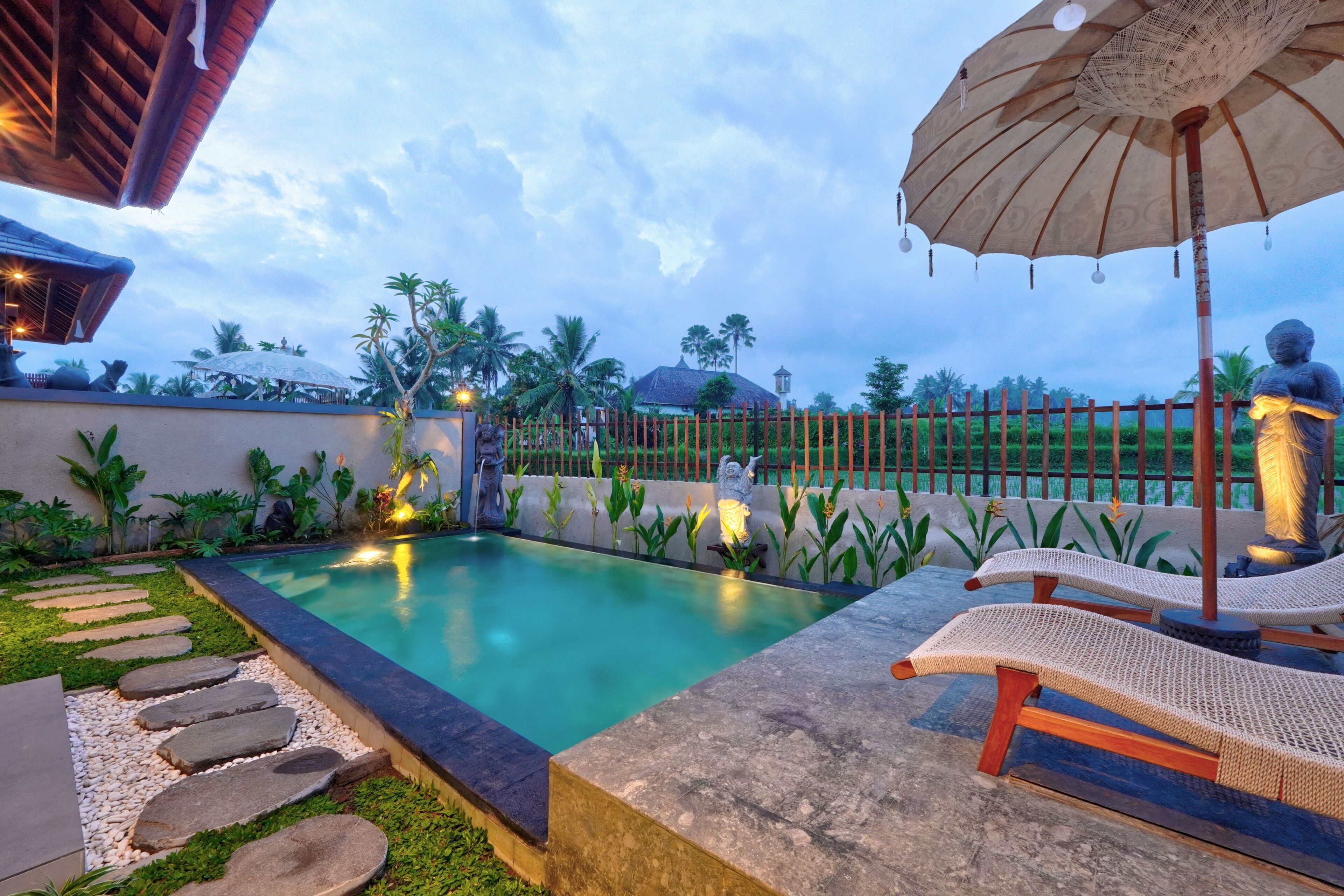 A swimming pool with stone steps leading to it, surrounded by a fence and palm trees.