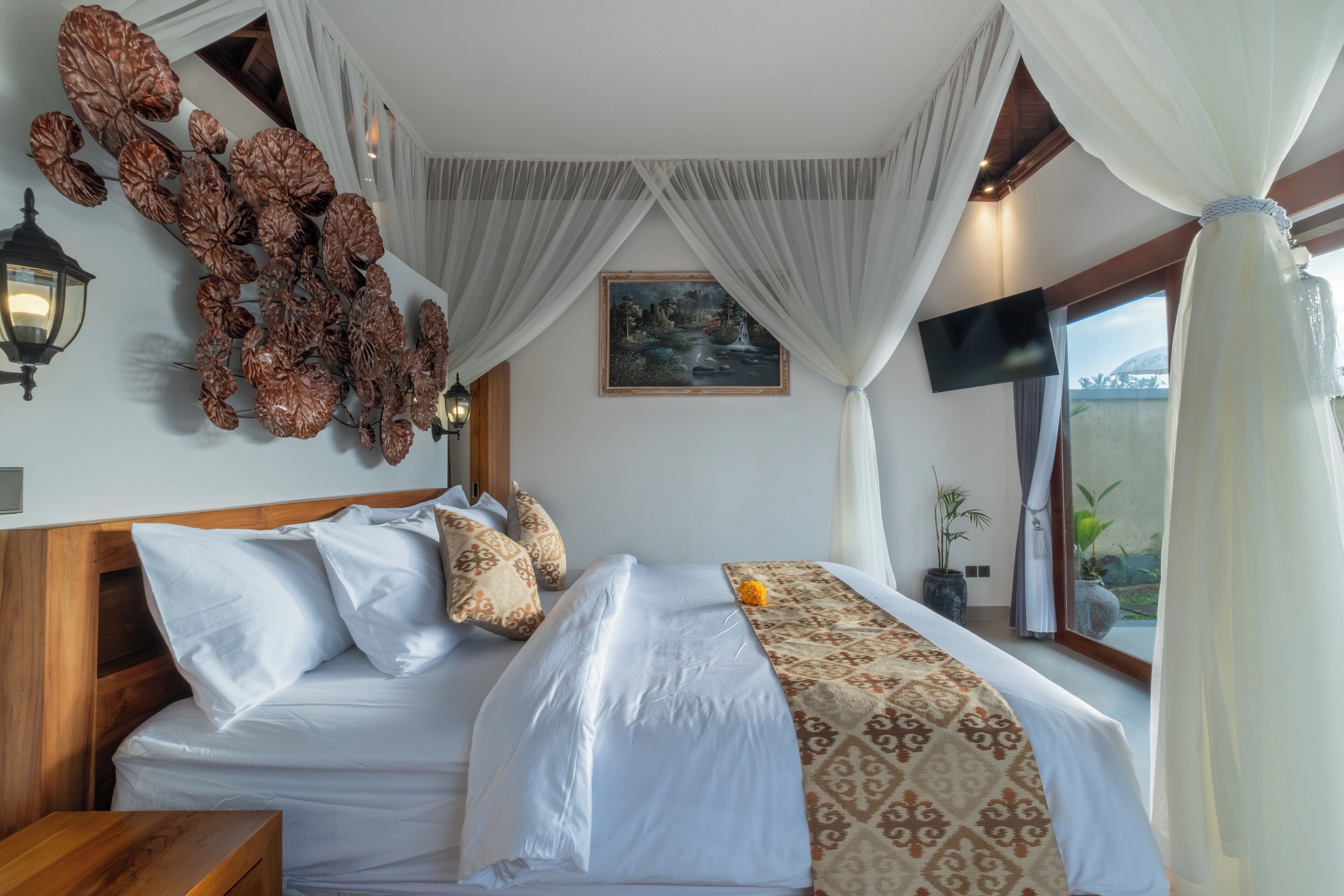 A bedroom with a large bed, white bedding, a decorative wall piece, a painting, and a window with curtains.