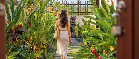 A pathway leading through a garden with tropical plants and a statue.