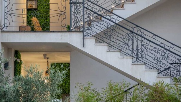 Um interior em vários níveis, com grades pretas elaboradas, uma parede verde com plantas e uma escadaria.