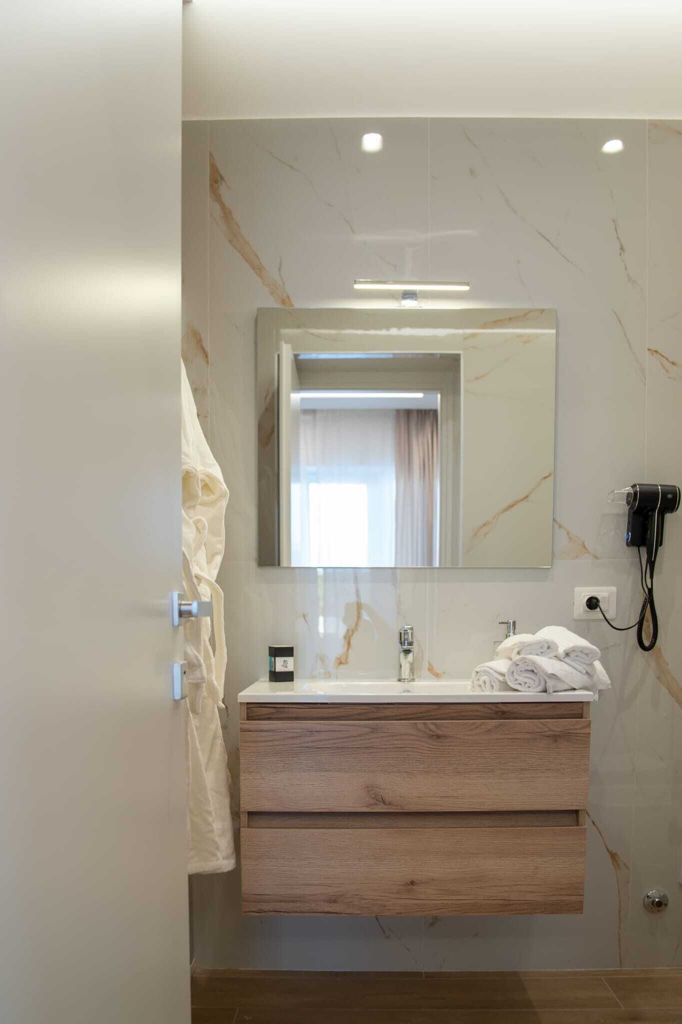 A modern bathroom with a marble vanity, a large mirror, and a hairdryer on the wall.