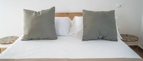 Una cama bien hecha con dos almohadas, un cabecero de madera y dos mesitas redondas con un diseño de estrellas.