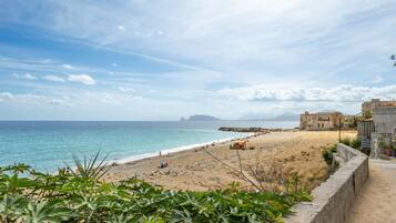 A coastal view with a beach, a stone wall, and buildings in the background.