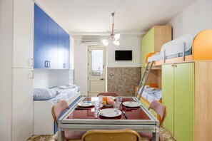 A compact room with bunk beds, a dining table with chairs, a TV mounted on the wall, and a door leading to another room. - Studio 'Little Casa Giovy' with Sea View, Wi-Fi and Air Conditioning (Palermo)