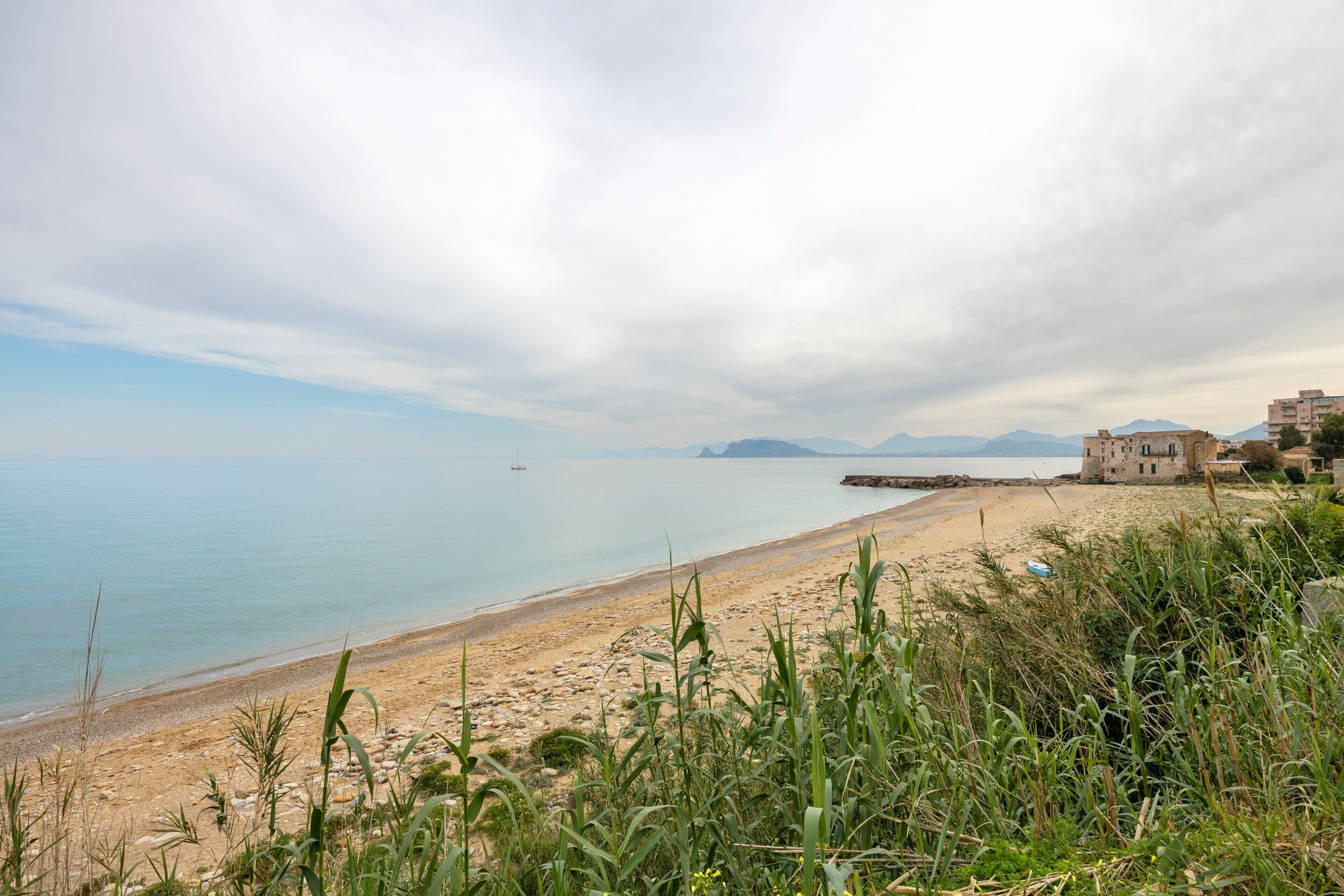Un paysage côtier comprenant une plage, une étendue d’eau et des montagnes à l’horizon.