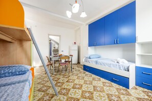 A room with a bunk bed, a desk with chairs, a refrigerator, and blue cabinets. - Studio 'Little Casa Giovy' with Sea View, Wi-Fi and Air Conditioning (Palermo)