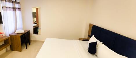 A hotel room with a bed, a desk, a chair, a ceiling fan, and a window with curtains.
