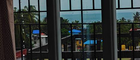 A view through a window with vertical bars, displaying a coastal area with buildings and palm trees.