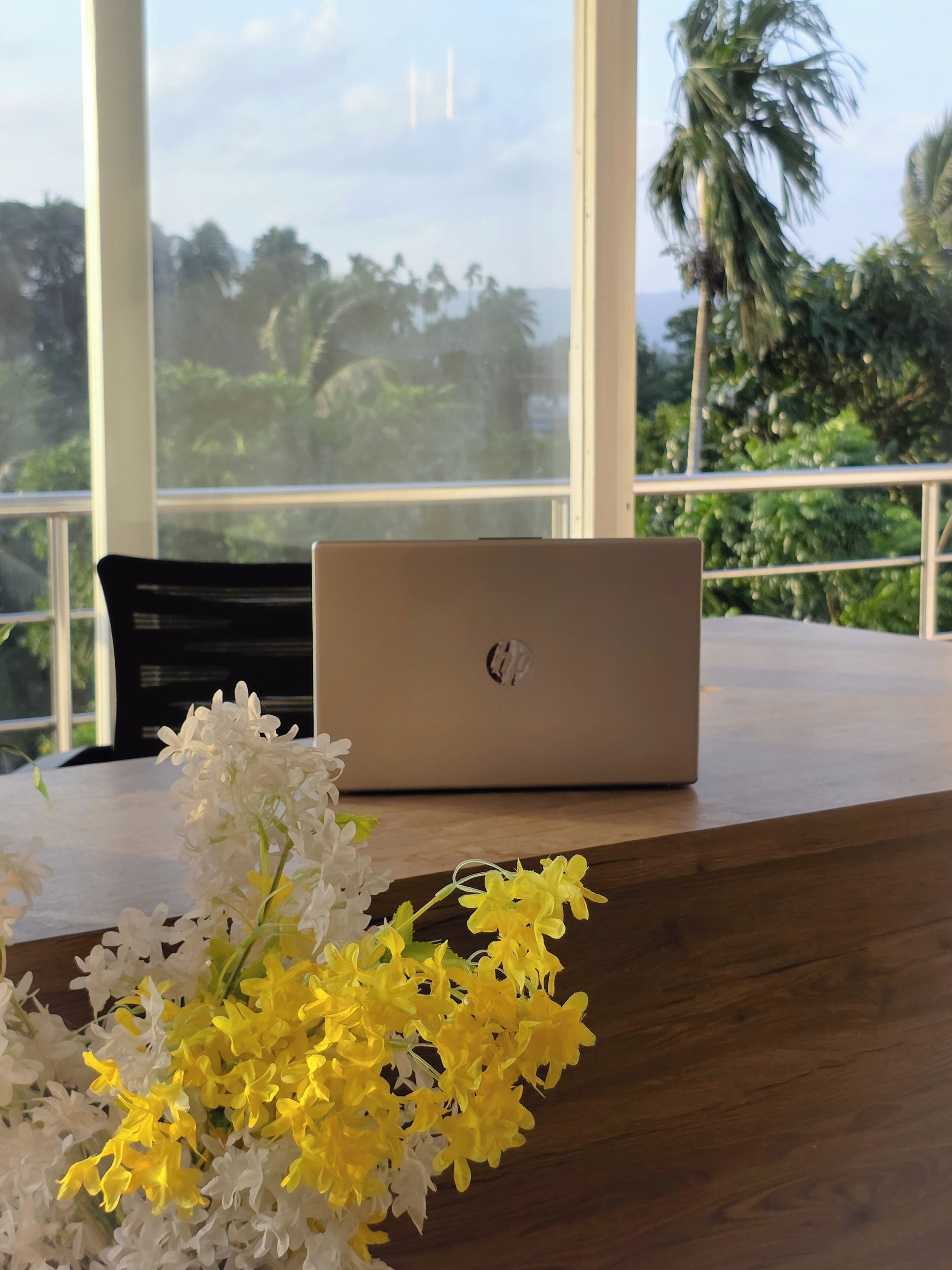 Een laptop op een houten tafel, met een bloevas op de voorgrond.