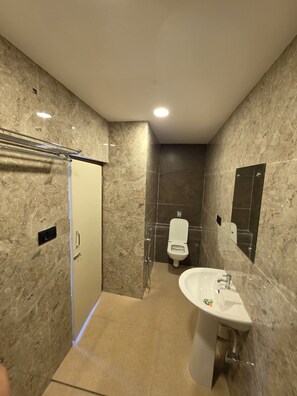 A modern bathroom with a marble wall, a shower, a toilet, and a sink. - Ross Harriet View (Port Blair)