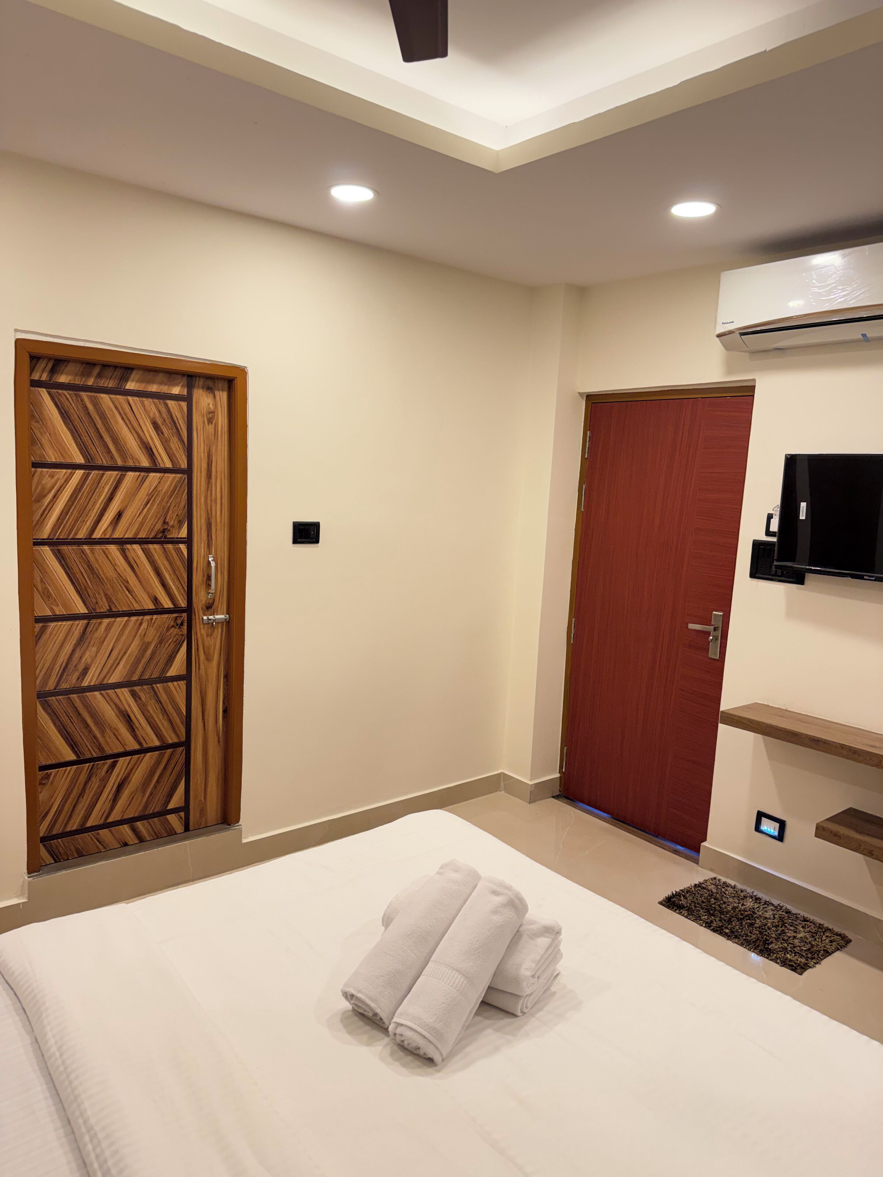 A hotel room with a bed, two doors, an air conditioning unit, and a TV.