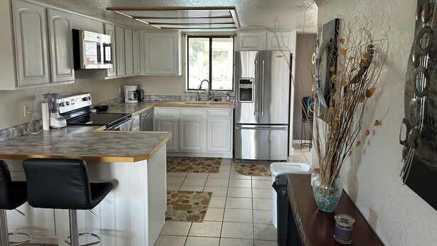 A modern kitchen with white cabinets, a stainless steel refrigerator, a built-in oven, and a coffee maker. - Charming, very quiet house (Lake Havasu City)
