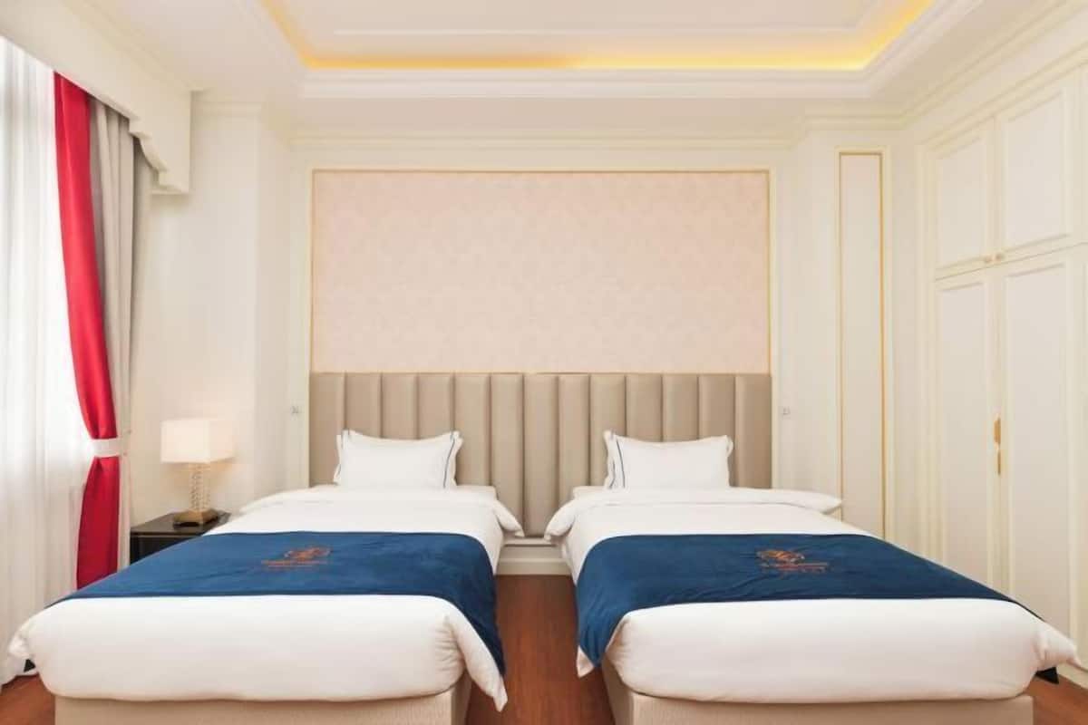 Una camera d'albergo con due letti, una testiera, un comodino con una lampada e una finestra con tende.