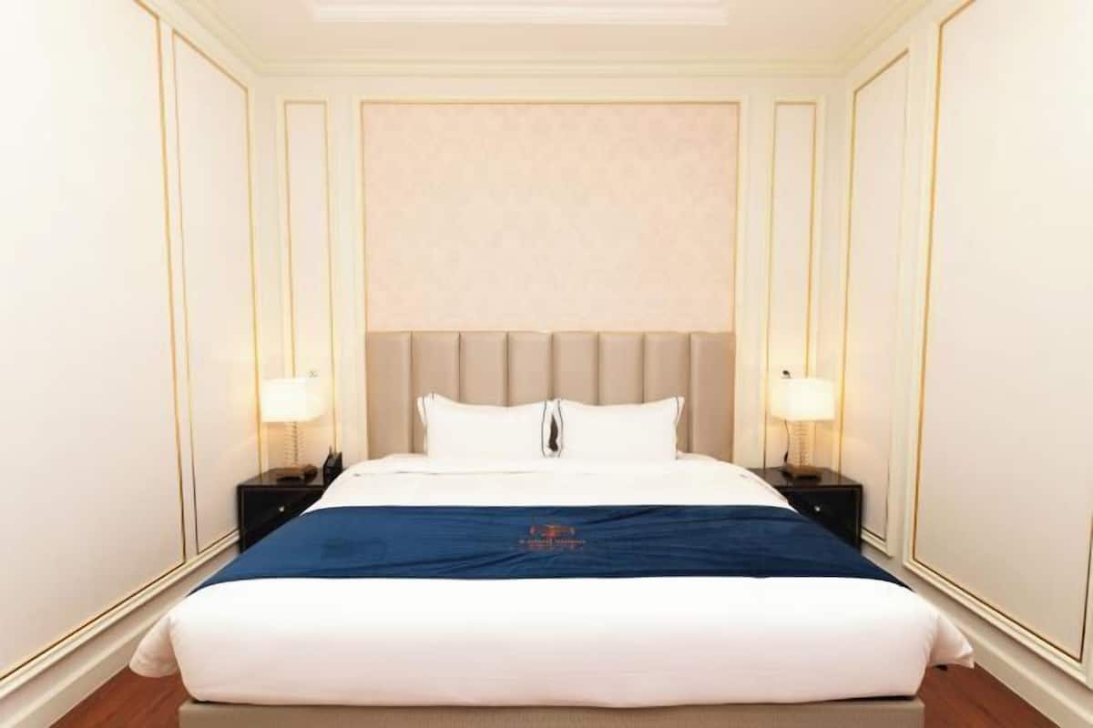 Un letto grande e ben rifatto, con un tocco di blu, affiancato da due comodini con lampade, in una stanza con pareti pannellate e una testiera semplice ed elegante.