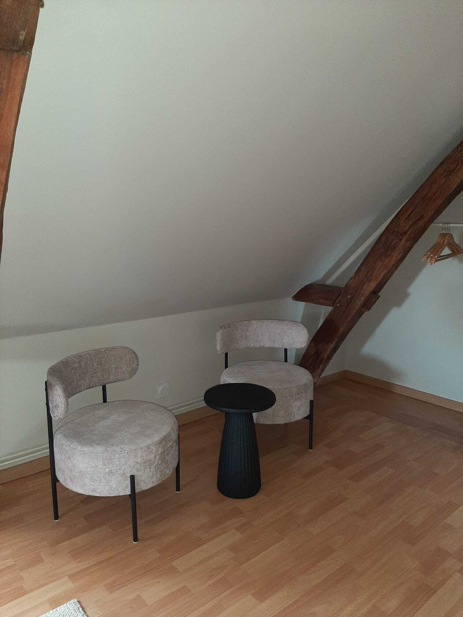 Een knus, klein kamertje met twee fauteuils en een ronde tafel, houten vloeren en een schuine plafond met zichtbare balken.