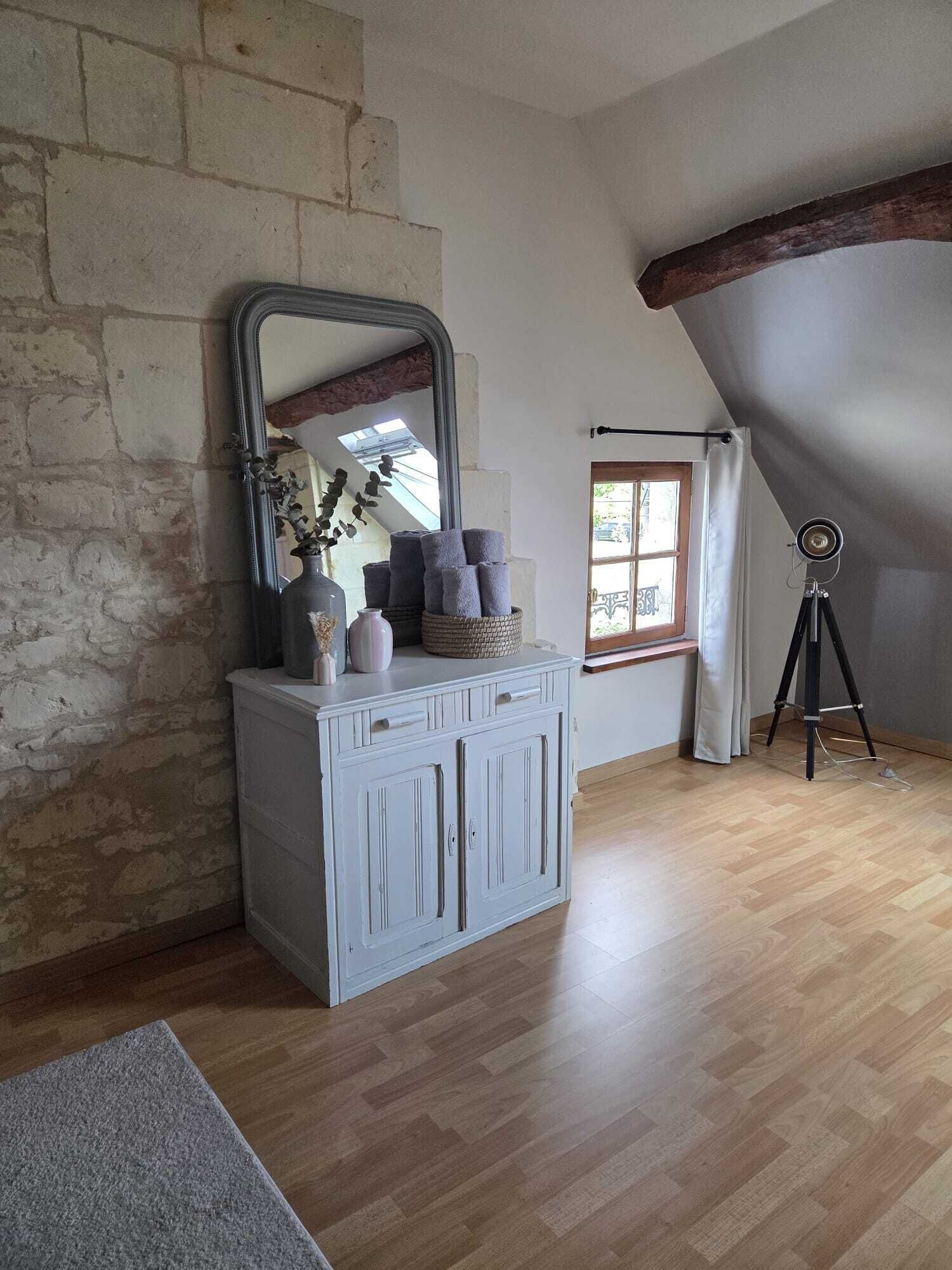 A room with a stone wall, a wooden ceiling, a white cabinet with a mirror, and a tripod lamp.