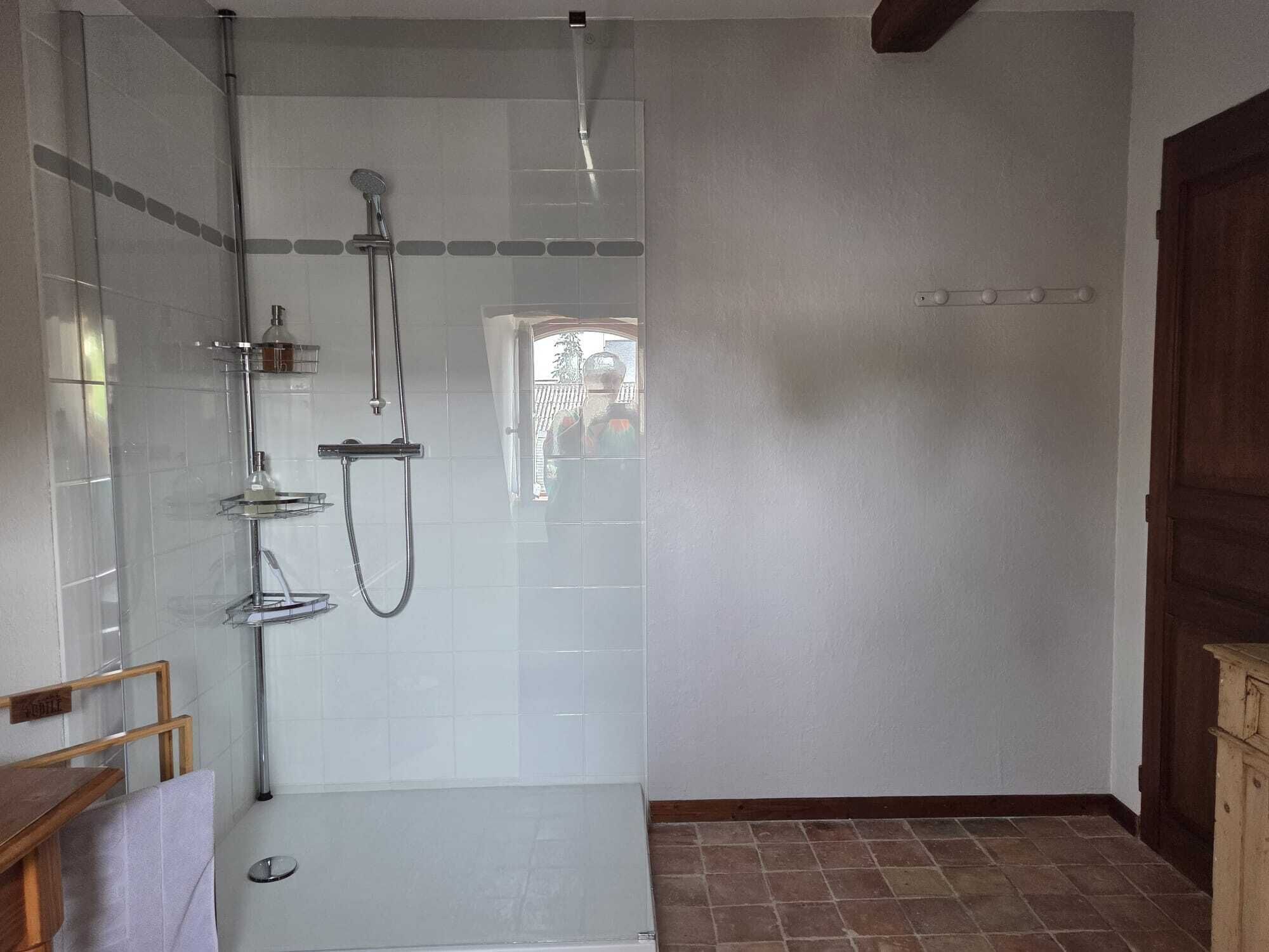 Una ducha a pie con paredes de vidrio, un banco de madera y suelo de baldosas.