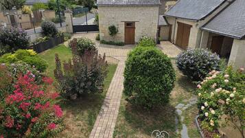 Un cortile con un vialetto lastricato, edifici in pietra e diverse piante fiorite.