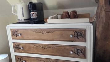 A wooden chest of drawers with a white top, a coffee maker, and a kettle on top.