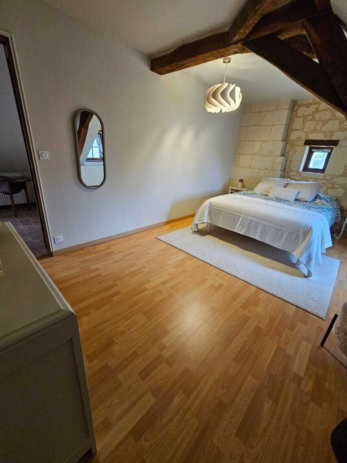 Una camera da letto con pavimento in legno, un letto con copripiumino bianco, uno specchio e un muro in pietra.