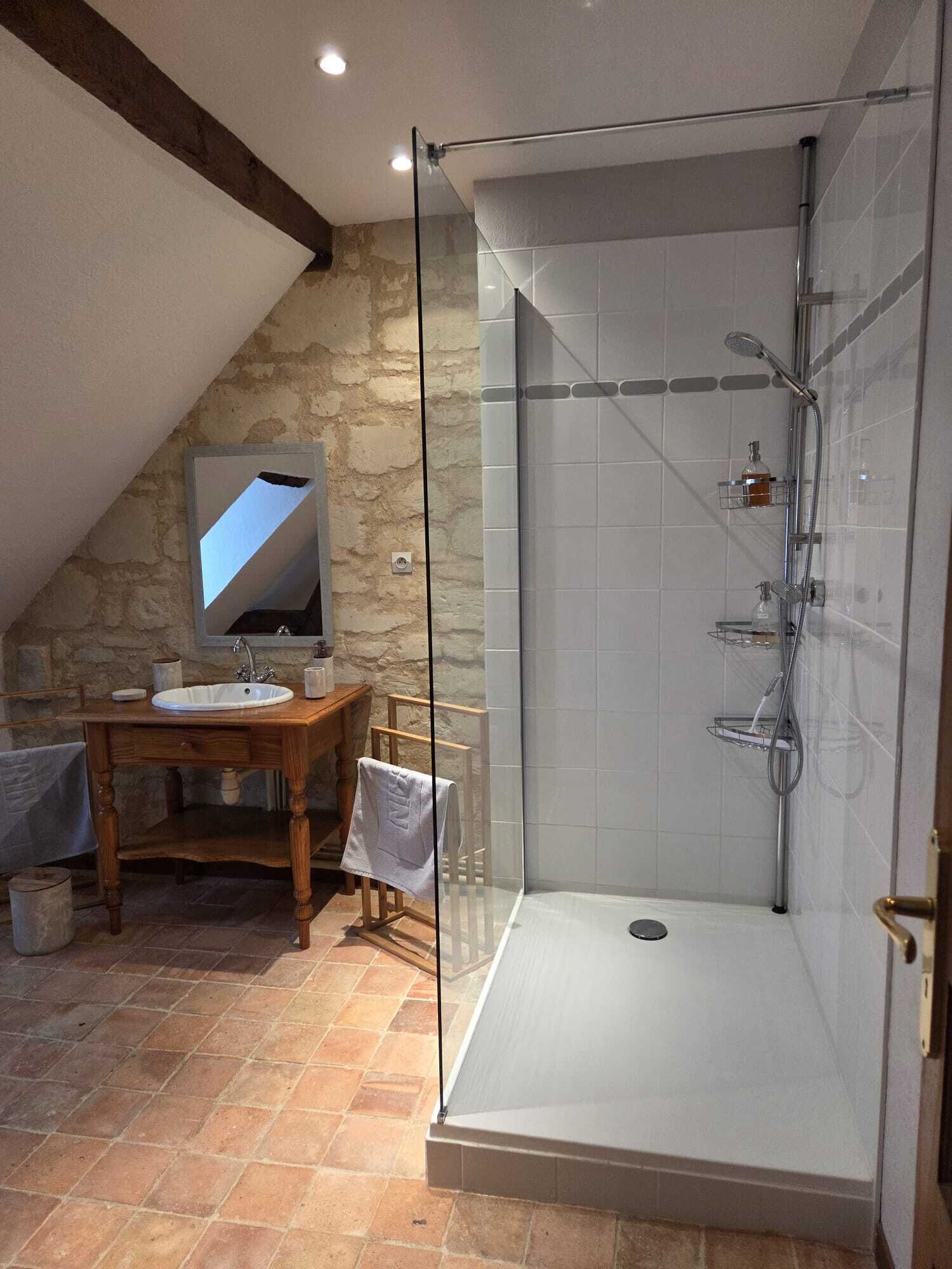 A bathroom with a stone wall, a wooden vanity with a sink, a glass shower enclosure, and a tiled floor.