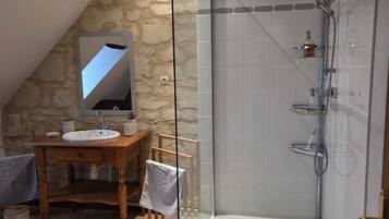 A bathroom with a stone wall, a wooden vanity with a sink, a glass shower enclosure, and a tiled floor.