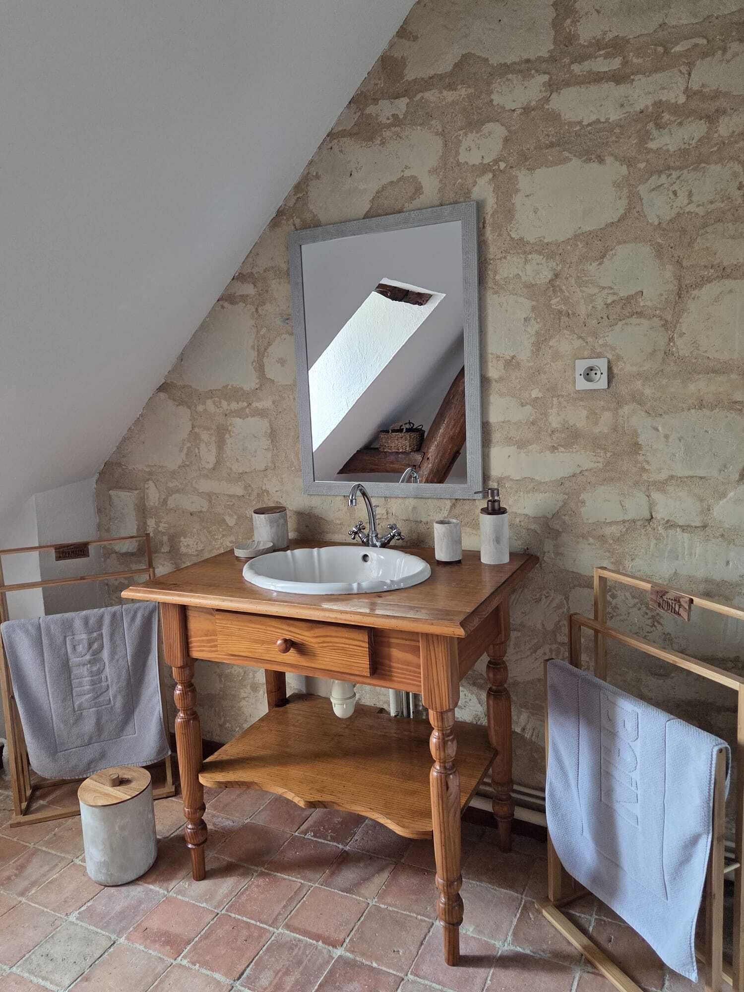 Un bany rústic amb un moble de tocador de fusta, un lavabo blanc i un mirall que reflecteix una prestatgeria de fusta.