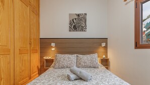 Una cama bien hecha con una colcha estampada, una obra de arte con cebra en la pared y un cabecero de madera con iluminación integrada.