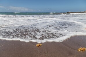 Een strand met golven, wier en een heldere lucht.