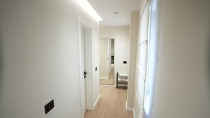 A narrow hallway with white walls and wooden flooring, leading to a room with a bed and a window. - Huqi Luxury Apartments (Tirana)