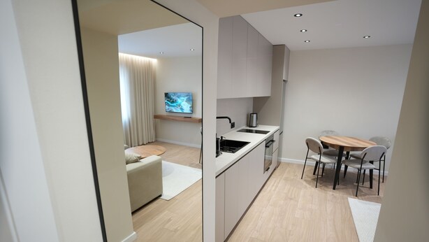 A modern kitchen with a dining area, wooden flooring, and a flat-screen TV. - Huqi Luxury Apartments (Tirana)