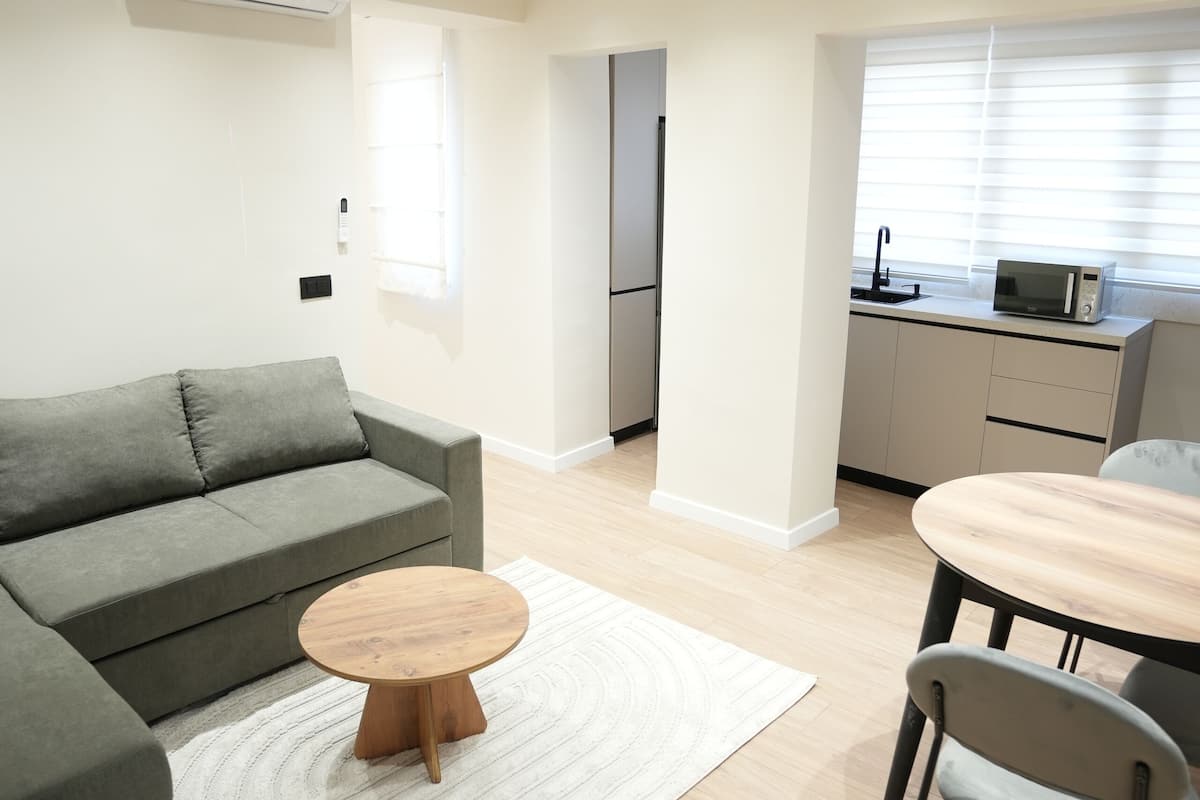 A modern living room with a grey sofa, a wooden coffee table, and a dining area with a white table and chairs.